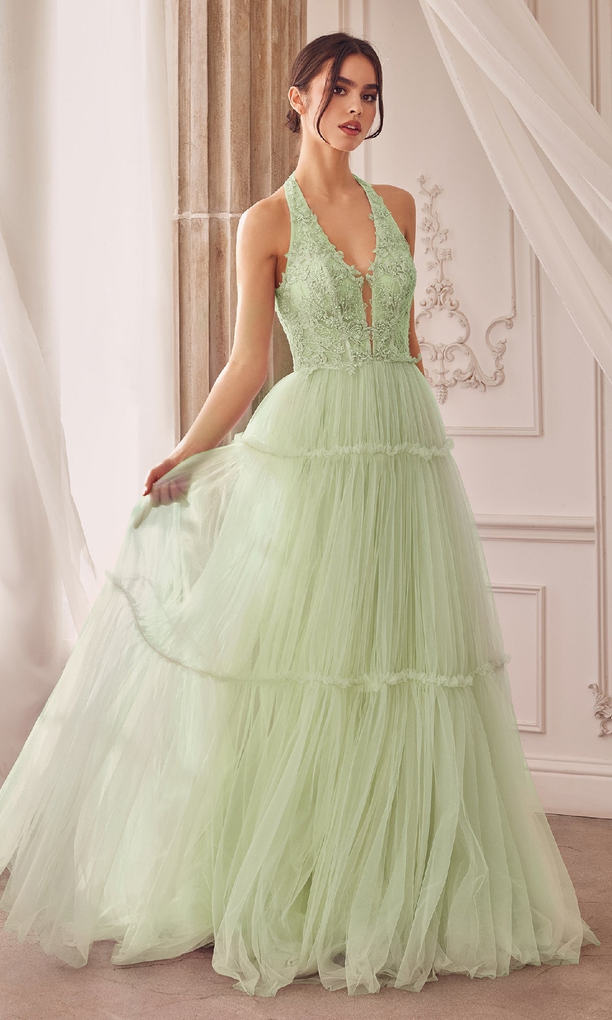 A woman stands indoors holding the skirt of her sleeveless, light green Lace-Halter Long A-Line Prom Dress A1206 with a floral-lace bodice.